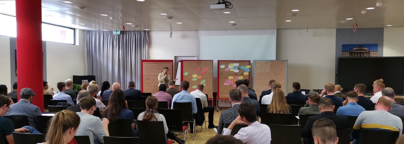 Ein Veranstaltungsraum voller Menschen, vorne präsentiert eine Frau.