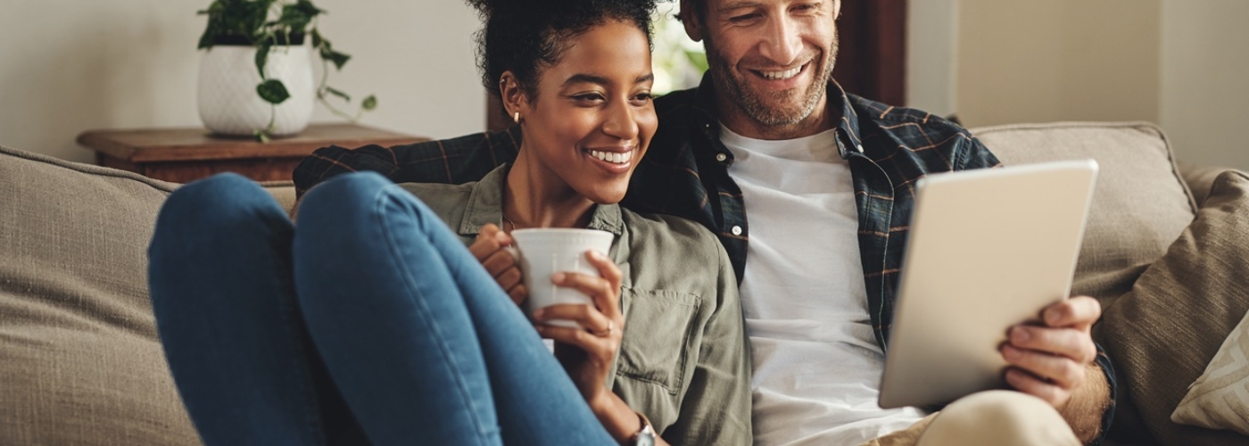 Eine Frau und ein Mann sitzen auf einem Sofa und schauen auf ein Tablet.