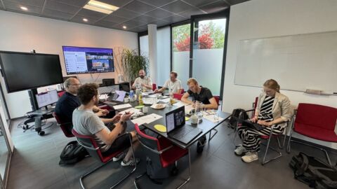 Fünf Männer und eine Frau sitzen an ienem Besprechungstisch.