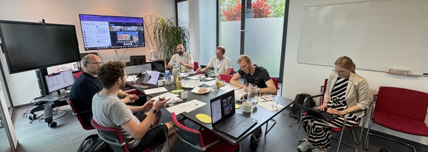 Fünf Männer und eine Frau sitzen an ienem Besprechungstisch.