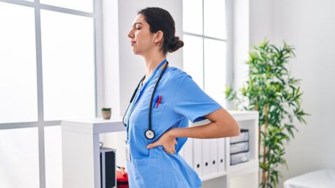 Eine Frau im blauen Kittel hält sich vor Schmerz den Rücken