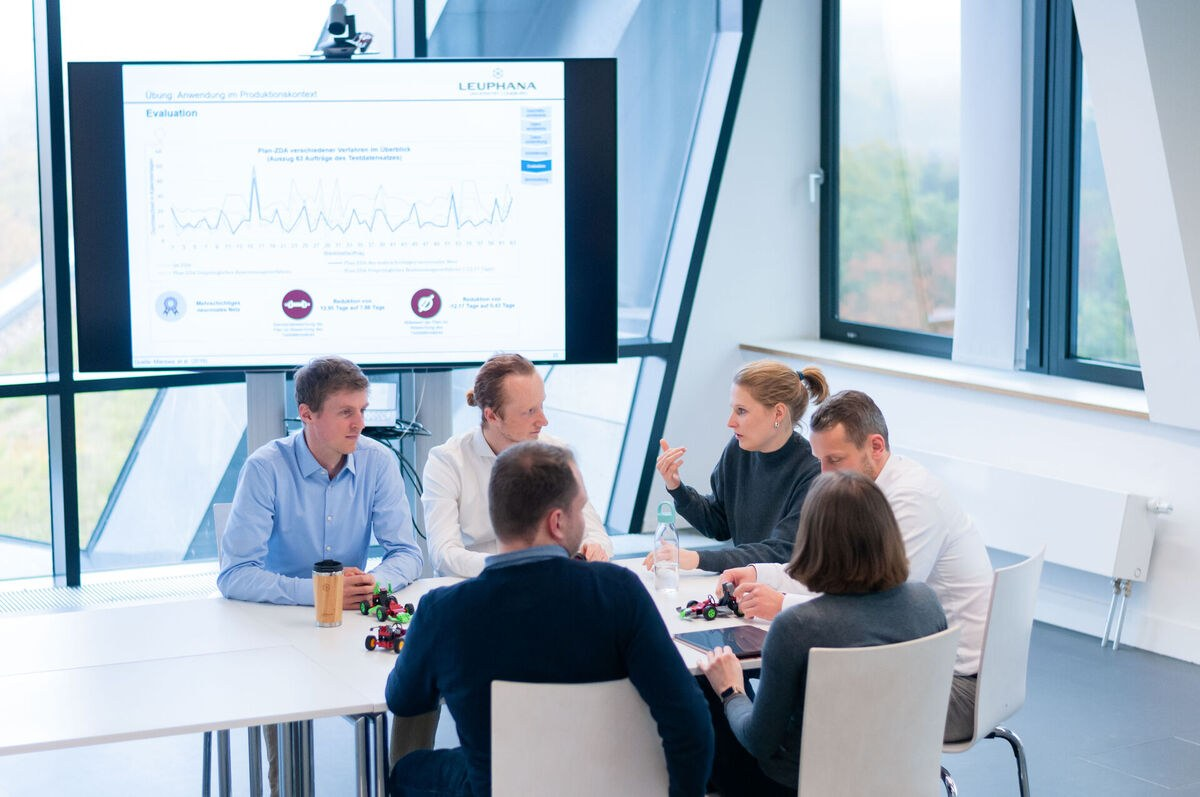 Sechs Personen sitzen in einem Büro an einem Konferenztisch und diskutieren