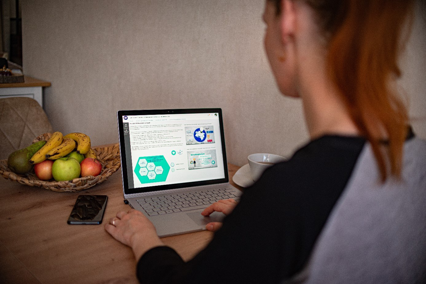 Frau sitzt an Tisch und bedient einen Laptop