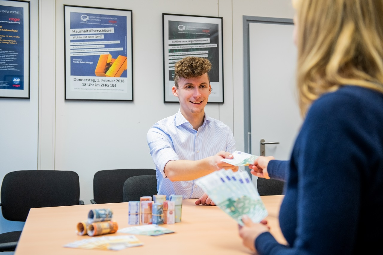 Zwei Personen sitzen an einem Tisch und übergeben Geld