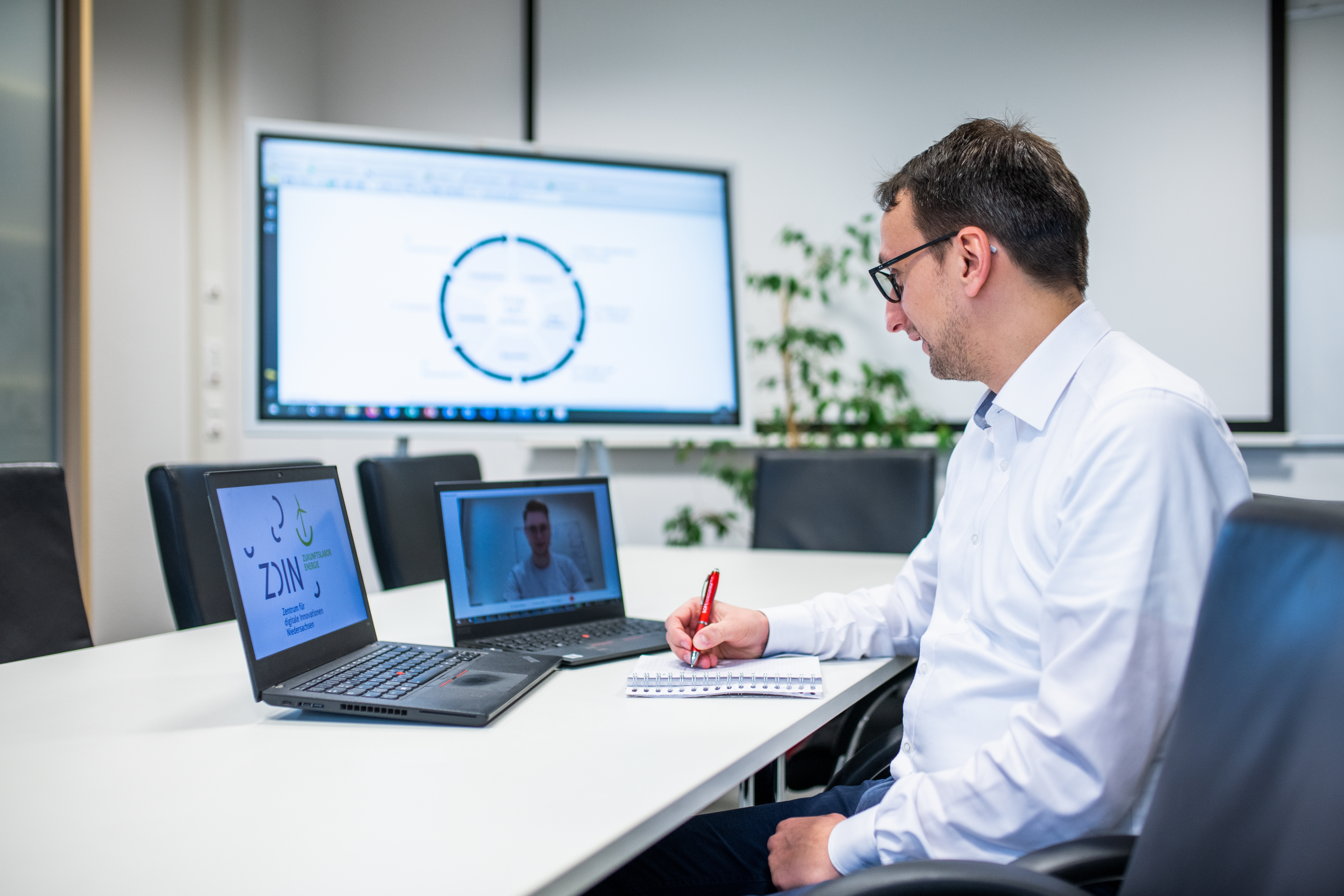 Mann sitzt an Tisch und bedient zwei Laptops