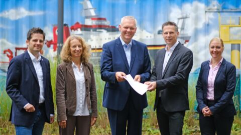 Fünf Personen blicken in die Kamera und lächeln.