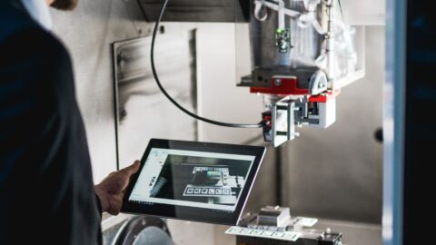 Person steht mit Tablet in der Hand vor einer Maschine