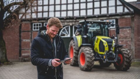 Mann steht mit Tablet vor einem Trecker.