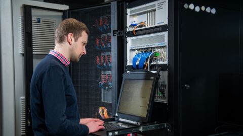 Mann steht bei einem Server und tippt etwas in die Tastatur