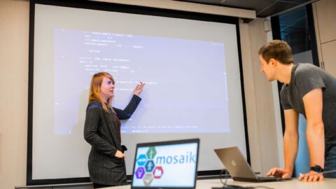 Frau erklärt einem Mann etwas an einer Leinwand