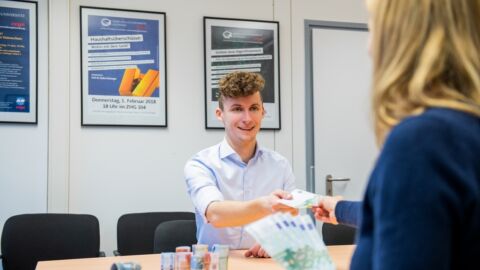 Ein Mann nimmt Geld von einer Frau an, während beide an einem Tisch sitzen.