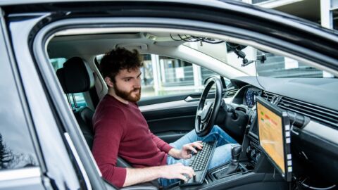 Mann sitzt in einem Auto und schaut auf zweiten Bildschirm