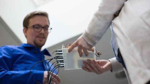 Frau hält Platte mit Kabeln, auf die ein Mann blickt