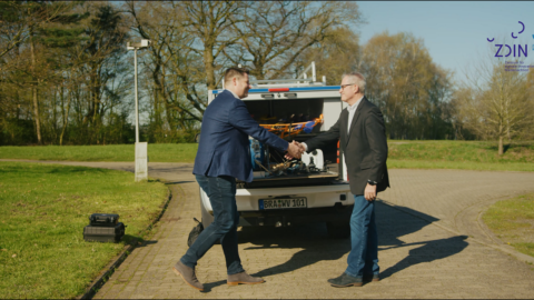 Zwei Männer geben sich die Hand vor einem Auto mit Equipment