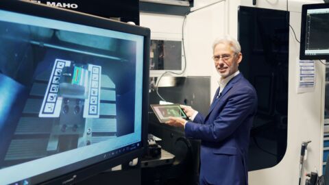 Mann hat Tablet in der Hand und sitzt vor Bildschirm