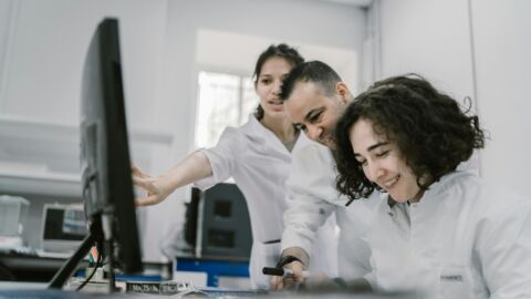 Zwei Frauen und ein Mann in weißen Kitteln arbeiten an einem Computer.