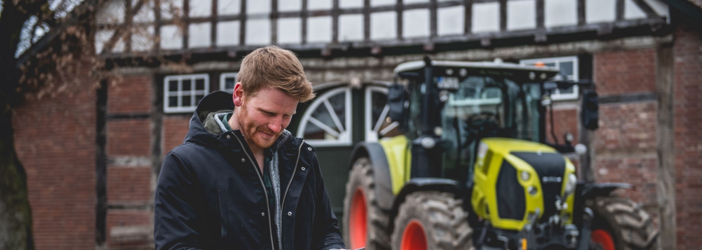 Mann steht mit Tablet vor einem Trecker.