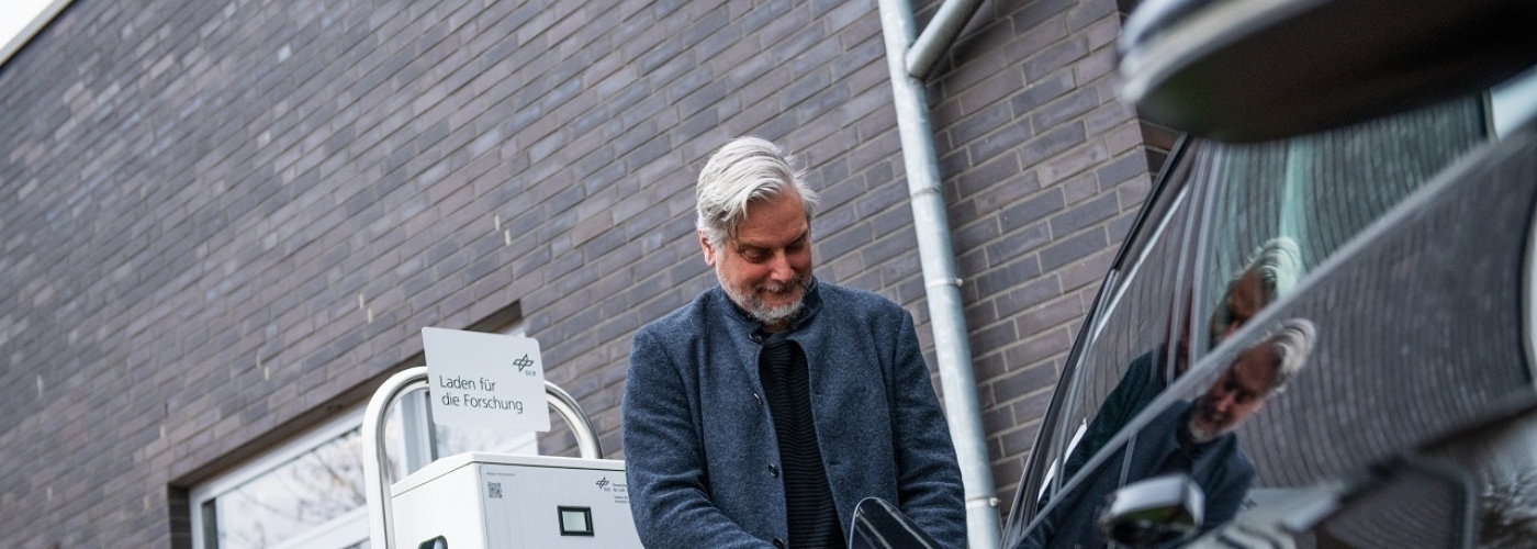 Mann steht an E-Ladesäule und lädt ein Auto auf