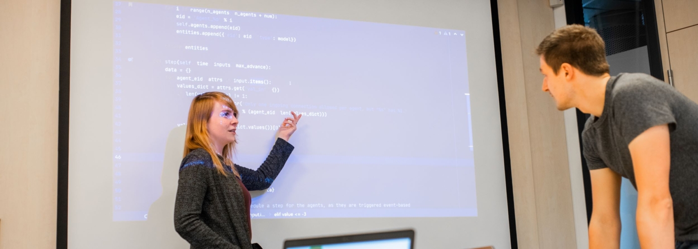 Frau erklärt einem Mann etwas an einer Leinwand