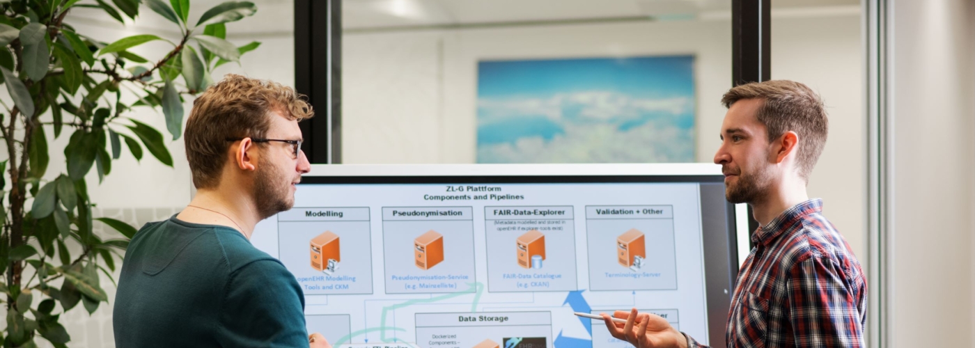 Zwei Männer stehen vor einem Bildschirm und sprechen miteinander