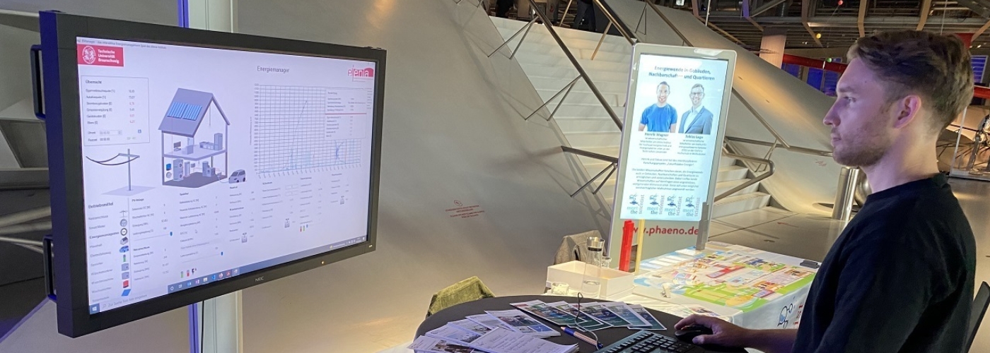 Ein Mann steht vor einem Bildschirm, auf dem ein Energiemanager für ein Hauses abgebildet ist