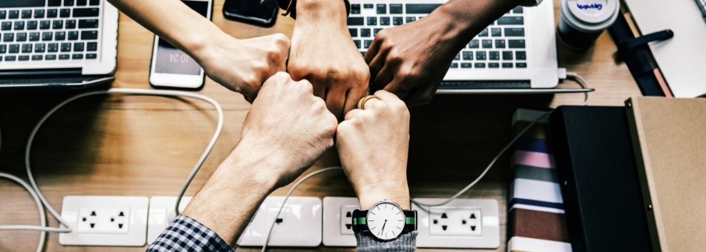Mehrere Personen berühren sich mit ihren Fäusten über einem Arbeitstisch