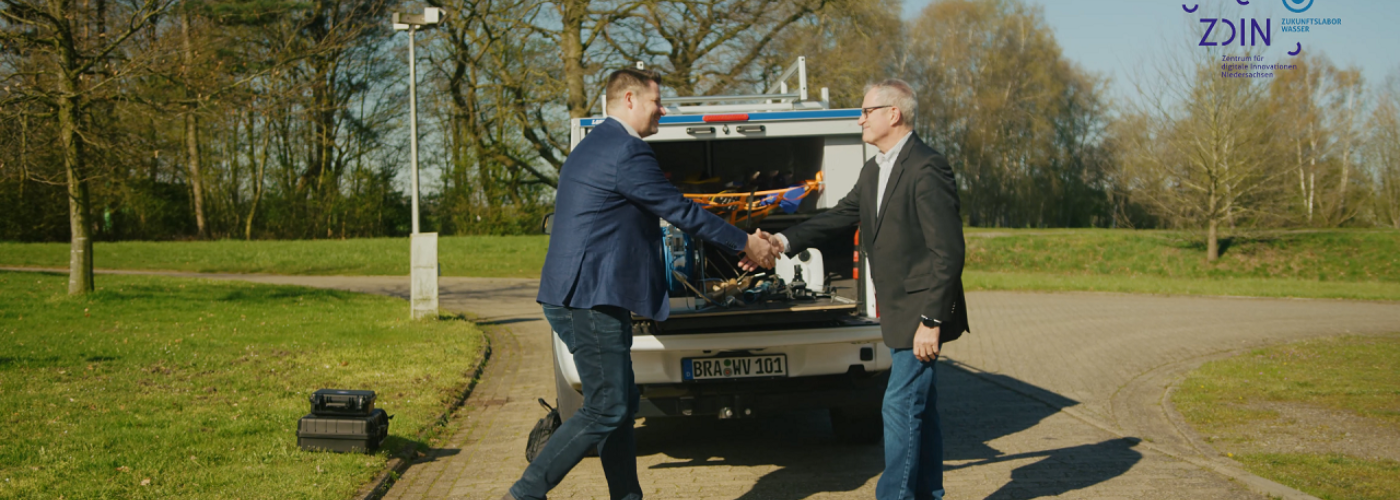 Zwei Männer geben sich die Hand vor einem Auto mit Equipment