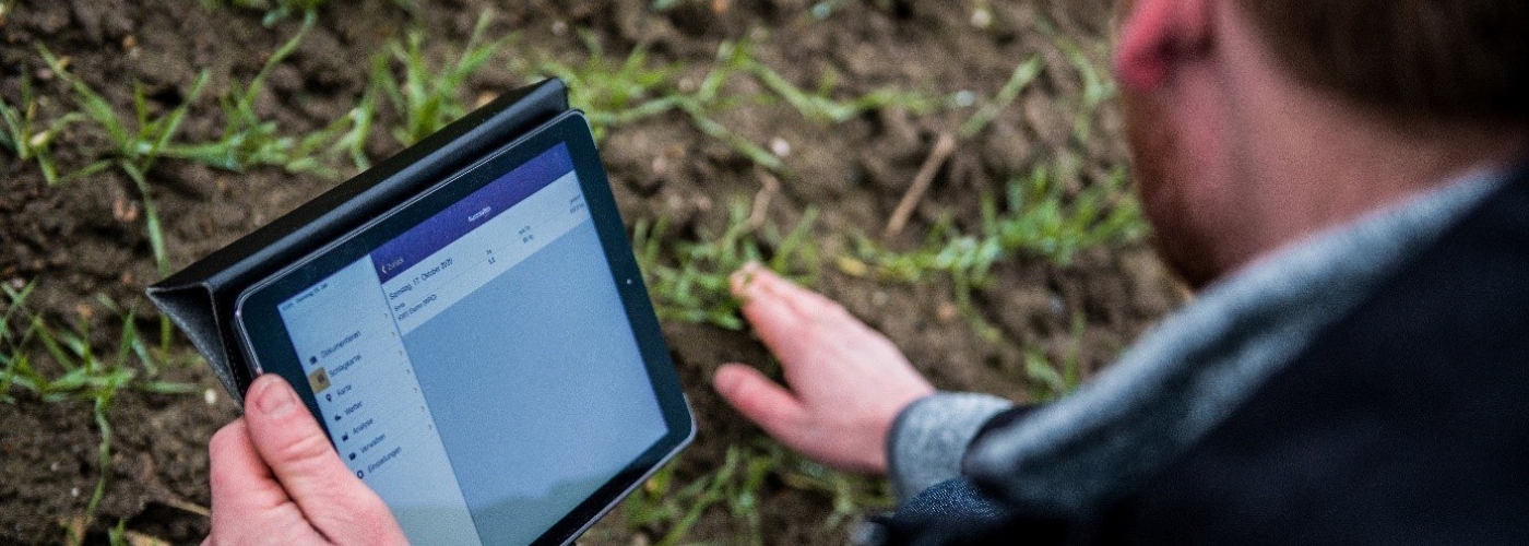 Mann steht mit Tablet auf Feld und berührt den Rasen