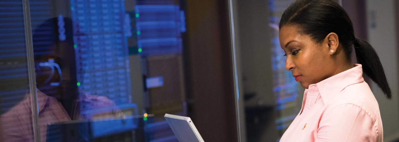 Frau steht in einem Serverraum und blickt auf einen Laptop