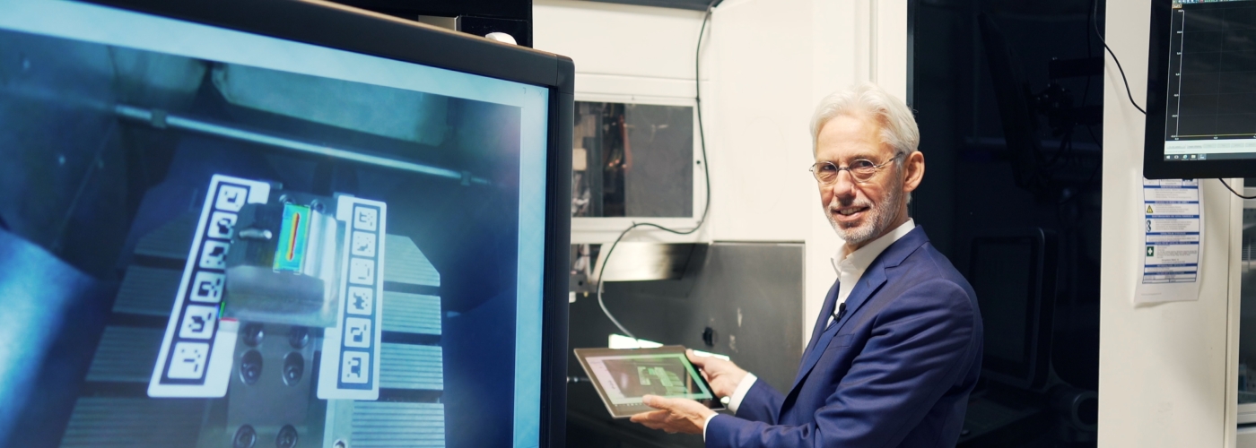 Mann hat Tablet in der Hand und sitzt vor Bildschirm