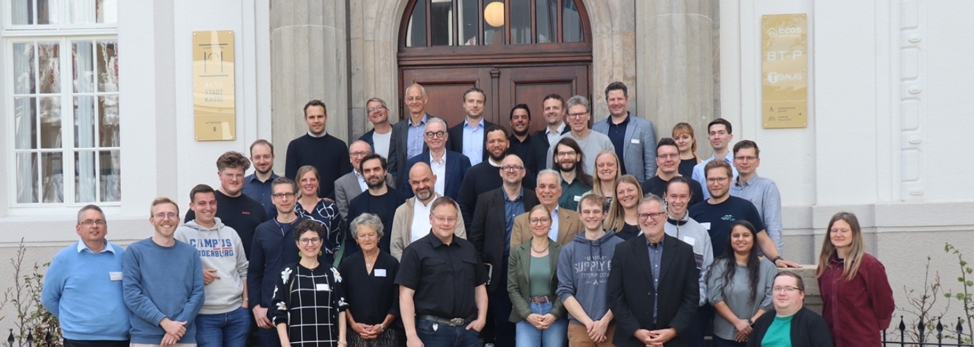 Eine Gruppe von Personen steht vor der Eingangstür eines Gebäudes.