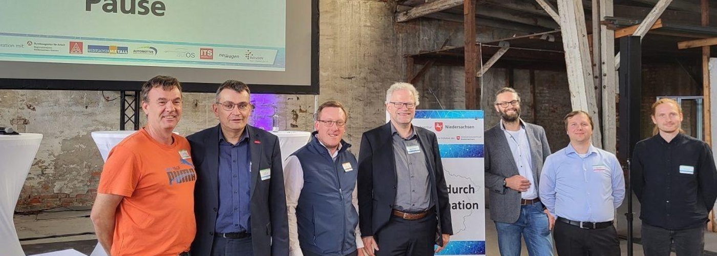 Eine Personengruppe steht vor einer Leinwand auf die "Pause" projiziert wird.