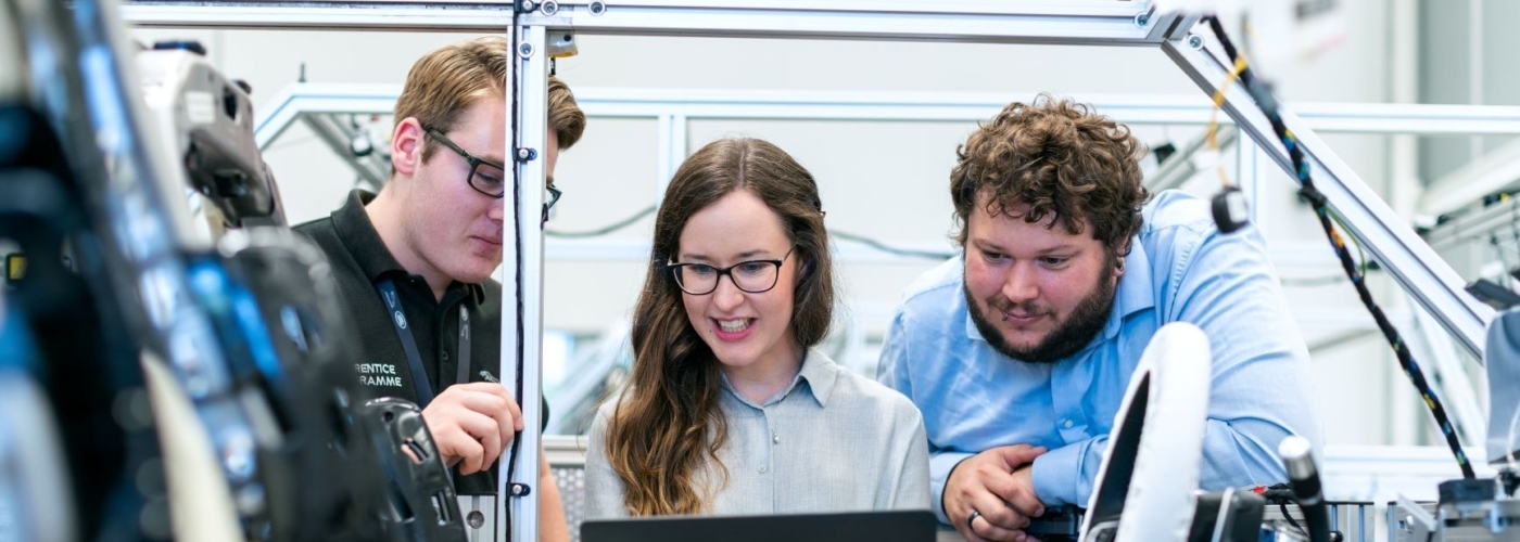 Drei Personen stehen mit einem Laptop bei einem Fahrzeug