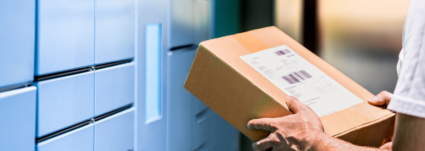 Eine Person hält ein Paket in den Händen und ist an einer Paketstation.